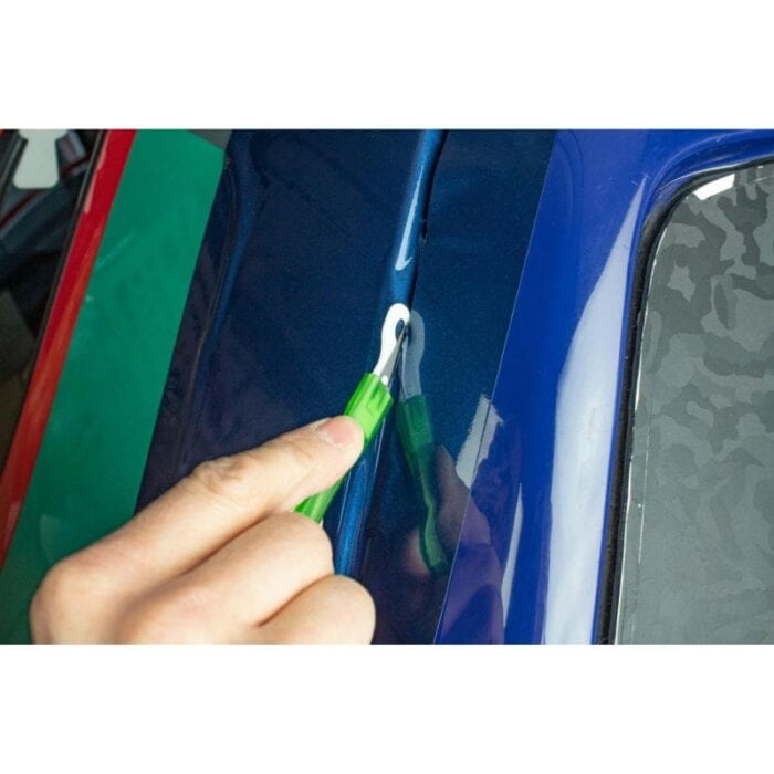 Une main manie avec expertise un coupe-vinyle WrapDefender vert pour l'emballage de voiture, coupant sans effort des feuilles de vinyle bleu et vert vibrantes qui sont appliquées en douceur sur ce qui semble être un panneau de voiture. - Tekalab