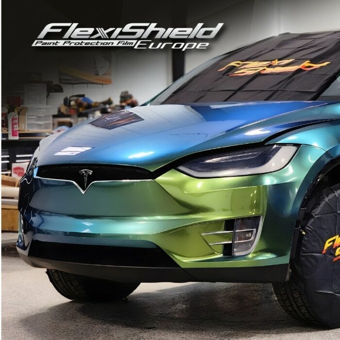 Une voiture Tesla multicolore et brillante, passant du vert au bleu, est garée à l'intérieur. L'image affiche en évidence le logo FlexiShield et le texte « Paint Protection Film Europe » en haut. La voiture est partiellement enveloppée de FLEXISHIELD Cosmétique PPF DM-04 Jungle pour la protection, soulignant la qualité supérieure du film utilisé. - Tekalab