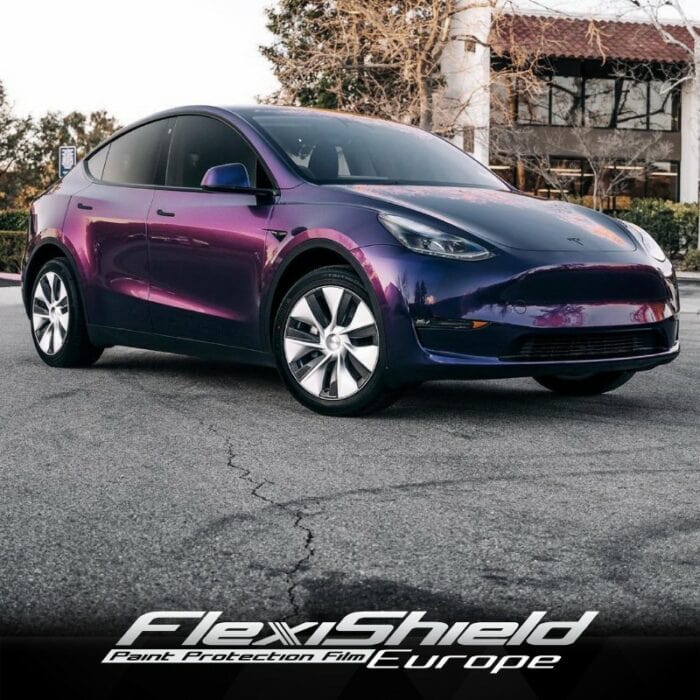 Une Tesla aux teintes violet foncé captivantes est garée dans une rue bordée d'arbres devant un bâtiment. L'image affiche le logo FlexiShield Paint Protection Film Europe en bas, mettant en valeur le FLEXISHIELD Cosmétique PPF DM-09 Gotham Purple alors qu'il émerge des ténèbres pour révéler une profondeur intrigante. - Tekalab