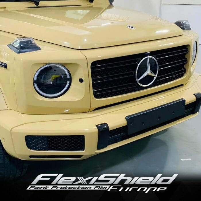 Gros plan sur la face avant d'un SUV de luxe beige, mettant en valeur sa calandre proéminente avec logo, ses phares circulaires et sa peinture brillante. La finition FLEXISHIELD Cosmétique PPF CL-12 Dune renforce son allure. Le texte FlexiShield PPF Europe est visible en bas de l'image. - Tekalab