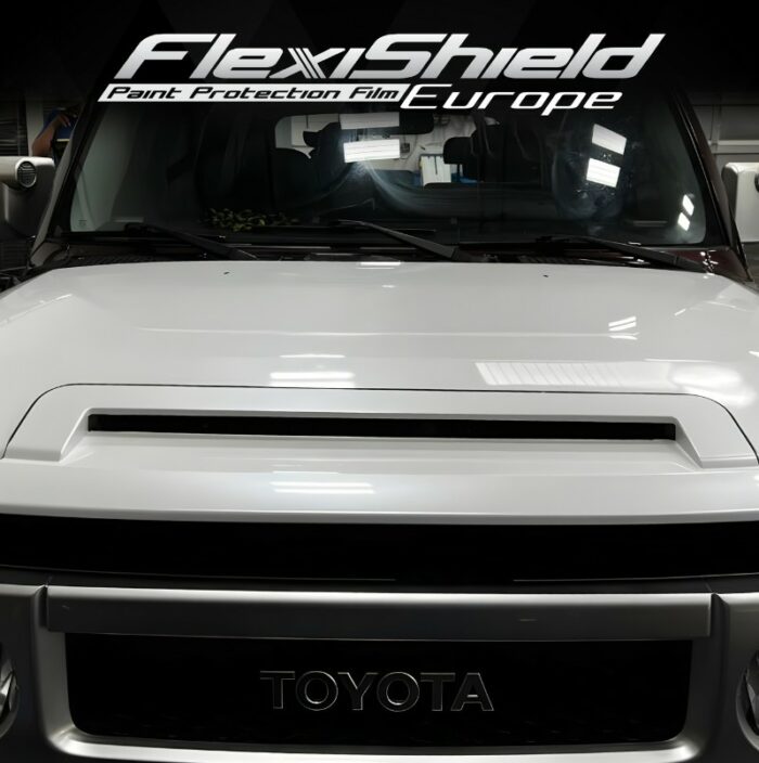 Une voiture Toyota blanche accentue son design lisse et élégant en mettant l'accent sur le capot affichant le logo FlexiShield Paint Protection Film Europe. La finition du véhicule est rehaussée par le FLEXISHIELD Cosmétique PPF HG-01 DIAMOND, ajoutant une couche supplémentaire d'élégance immaculée. - Tekalab