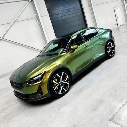 Une voiture élégante, dun vert métallisé et au design moderne, brille dans un showroom spacieux. Dotée daccents noirs et de jantes élégantes, elle est protégée par FLEXISHIELD Cosmétique PPF TP-04 Moon Beam 2.0 et présentée en biais contre un mur blanc aux éléments industriels subtils. - Tekalab