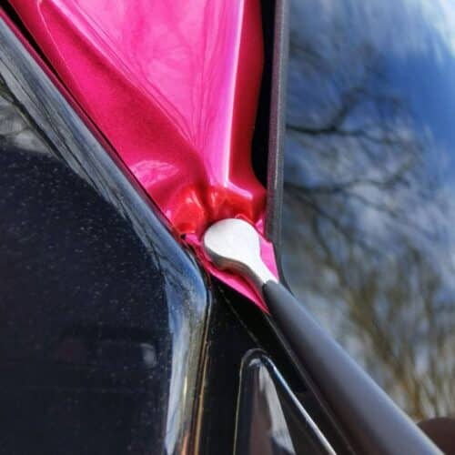 Une pelle WrapTweezer, un objet recouvert de tissu avec un point dancrage métallique, reflète des branches darbres et un ciel bleu sur une surface noire brillante à lextérieur. - Tekalab