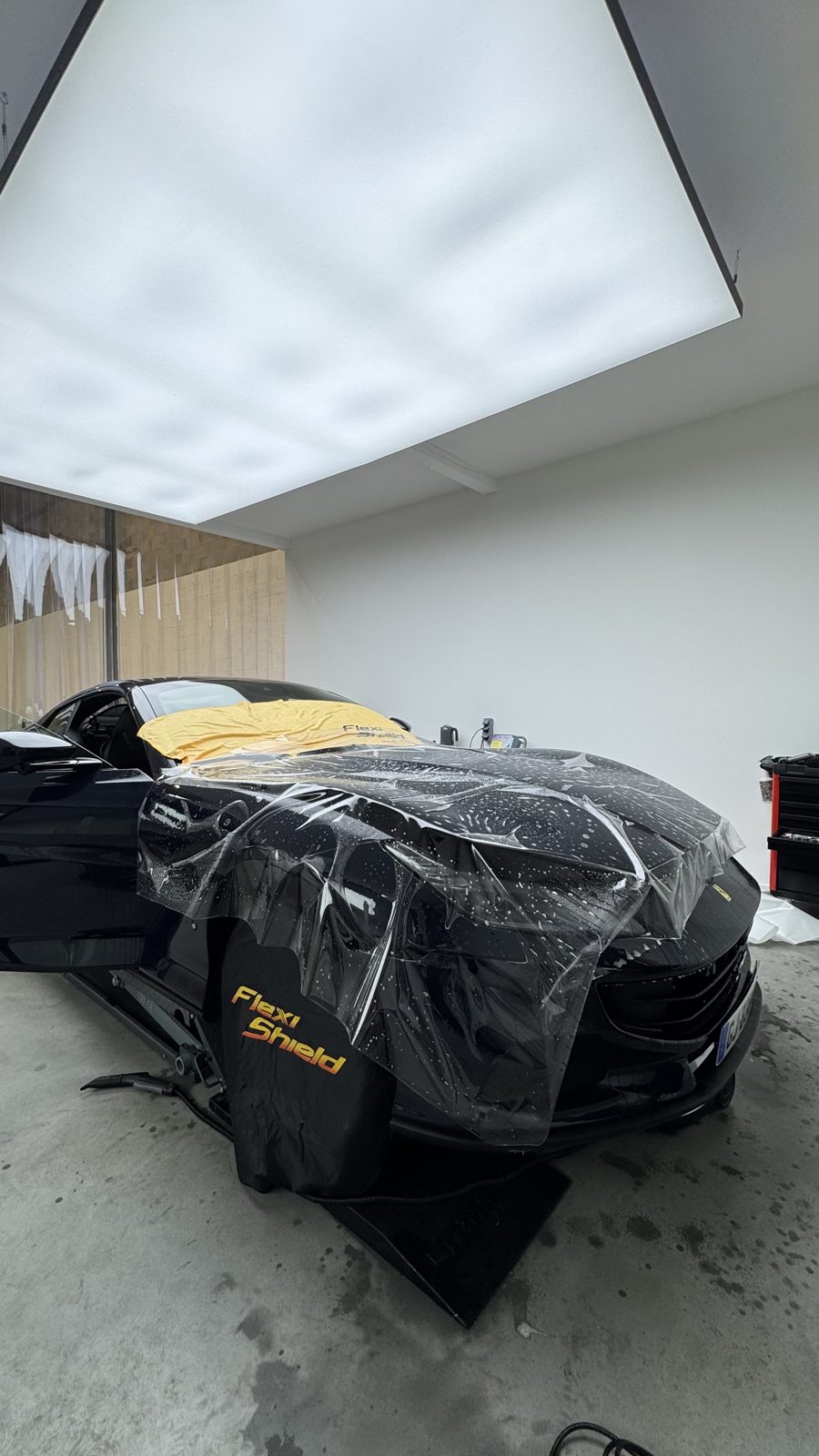 Pose d'un film de protection PPF sur la face avant d'une voiture, en atelier